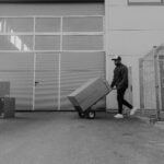 Black and white photo of a delivery worker moving packages outside a warehouse.